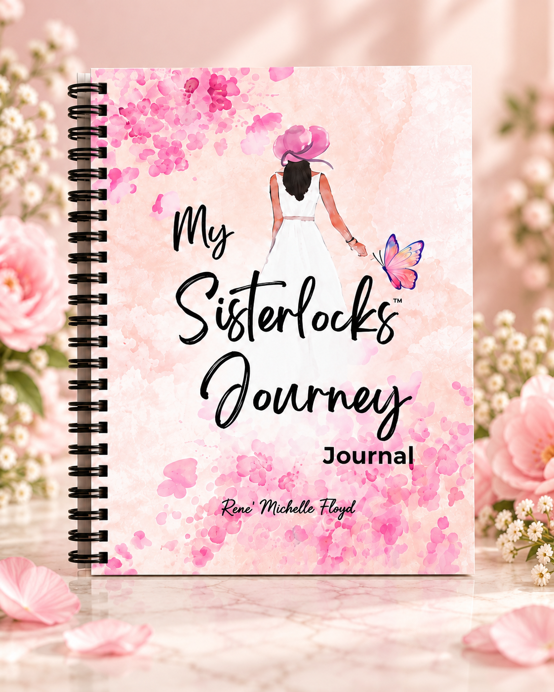 My Sisterlocks Journey Journal spiral-bound cover displayed upright in a soft pink floral setting.
